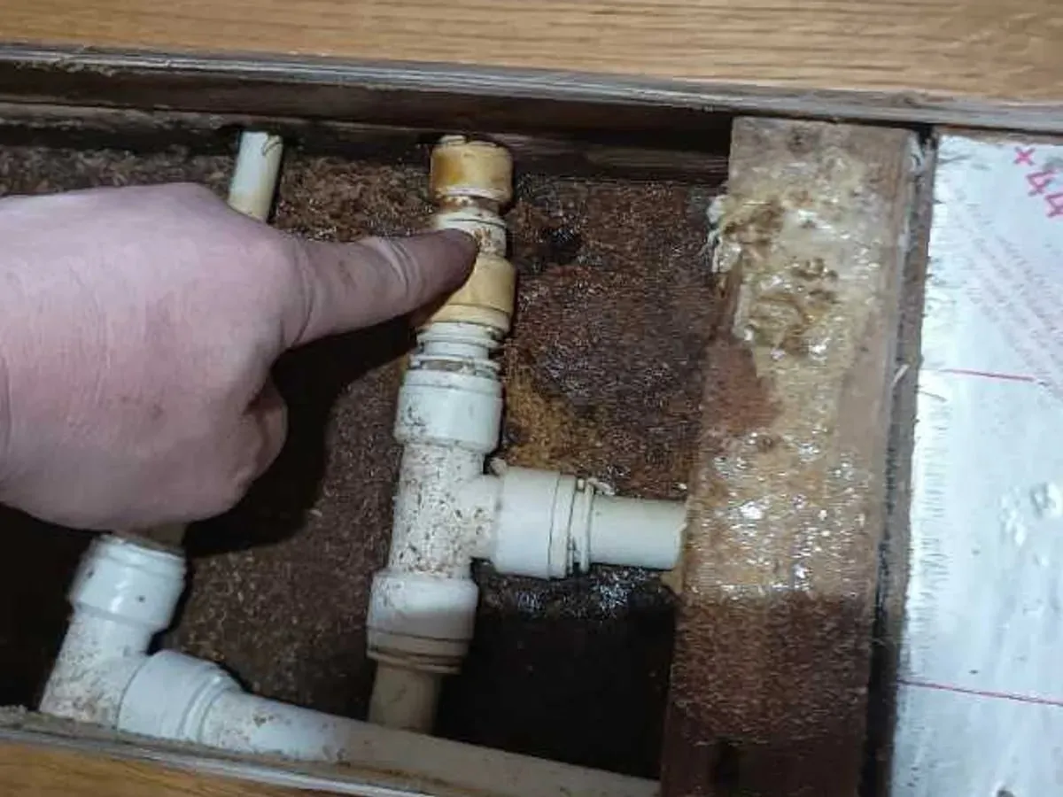 Finger pointing at a cracked white push-fit fitting under the floor