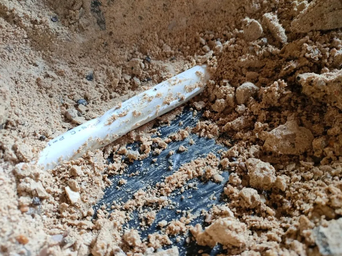 Damaged white plastic pipe lying in broken, damp screed