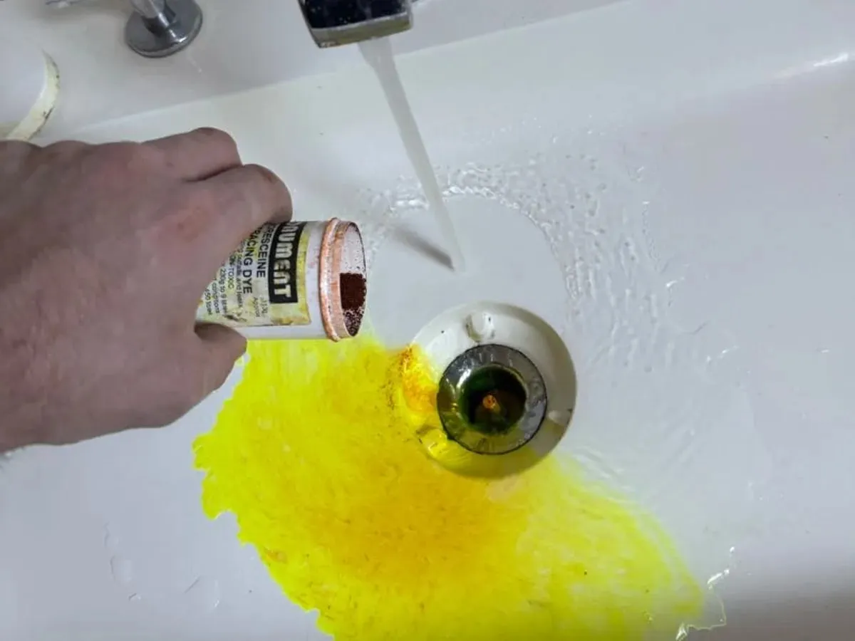 Yellow leak dye being poured into a bath waste