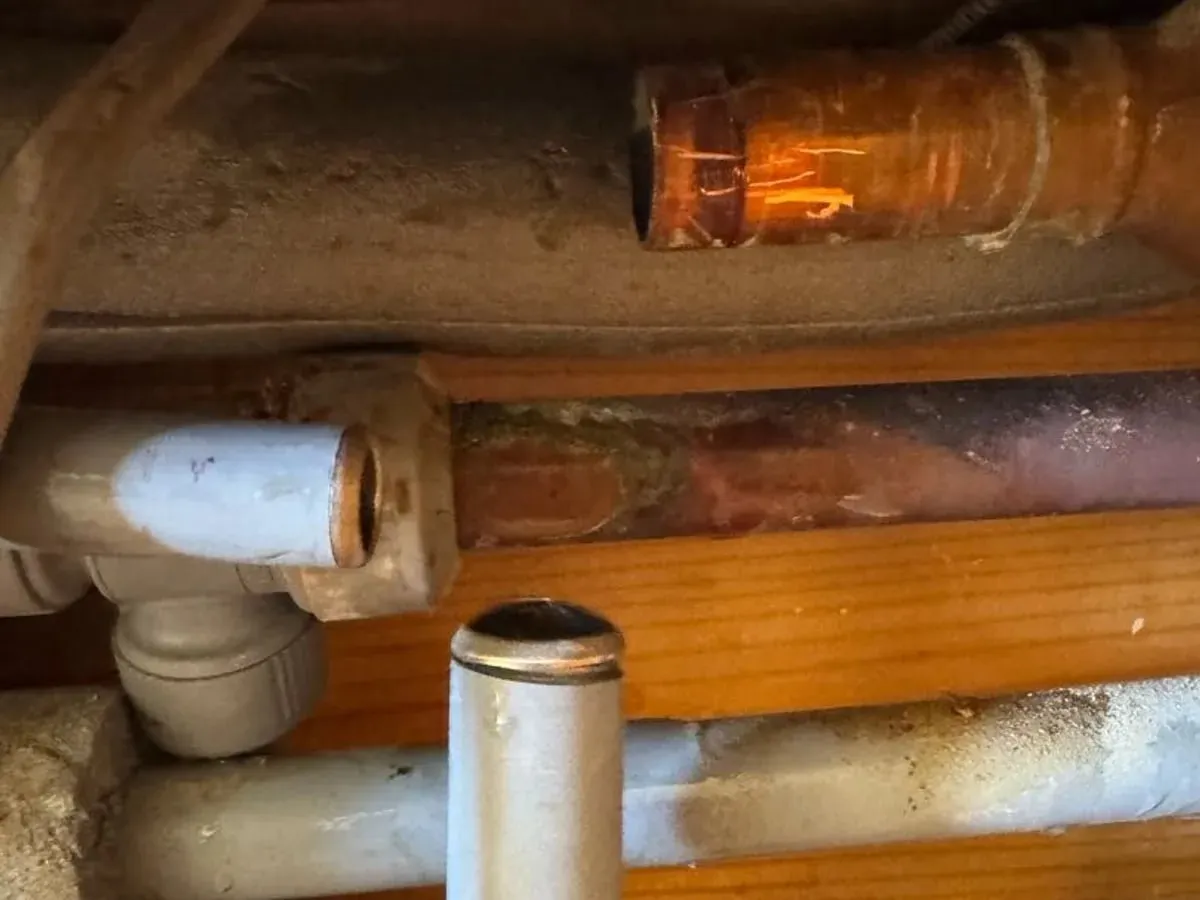 Corroded copper and plastic T-piece fitting behind the opened wall