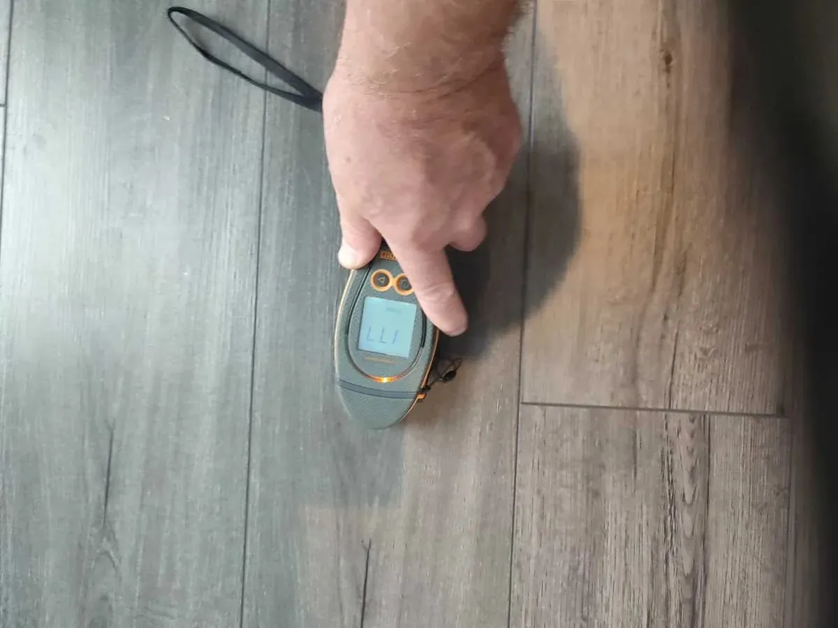 Hand pressing a moisture meter onto laminate flooring