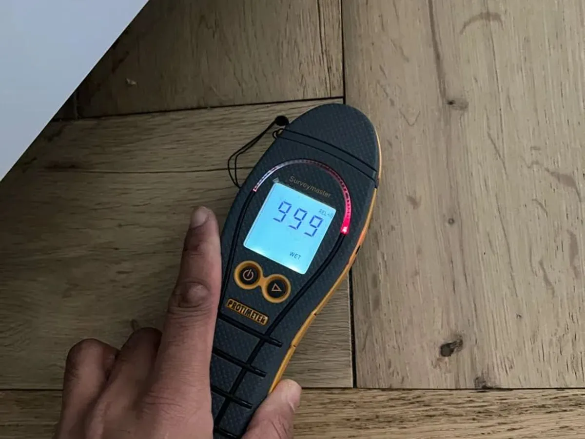 Moisture meter pressed to a wooden floor showing a high reading