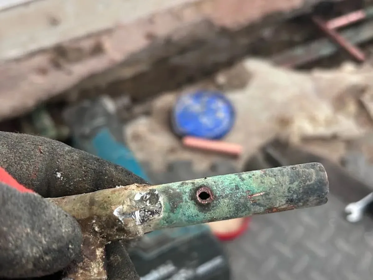 Hand holding a removed copper pipe section with a hole corroded through it