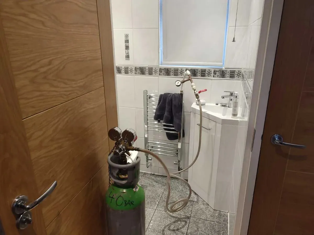 Tracer gas cylinder with a hose connected in a bathroom doorway