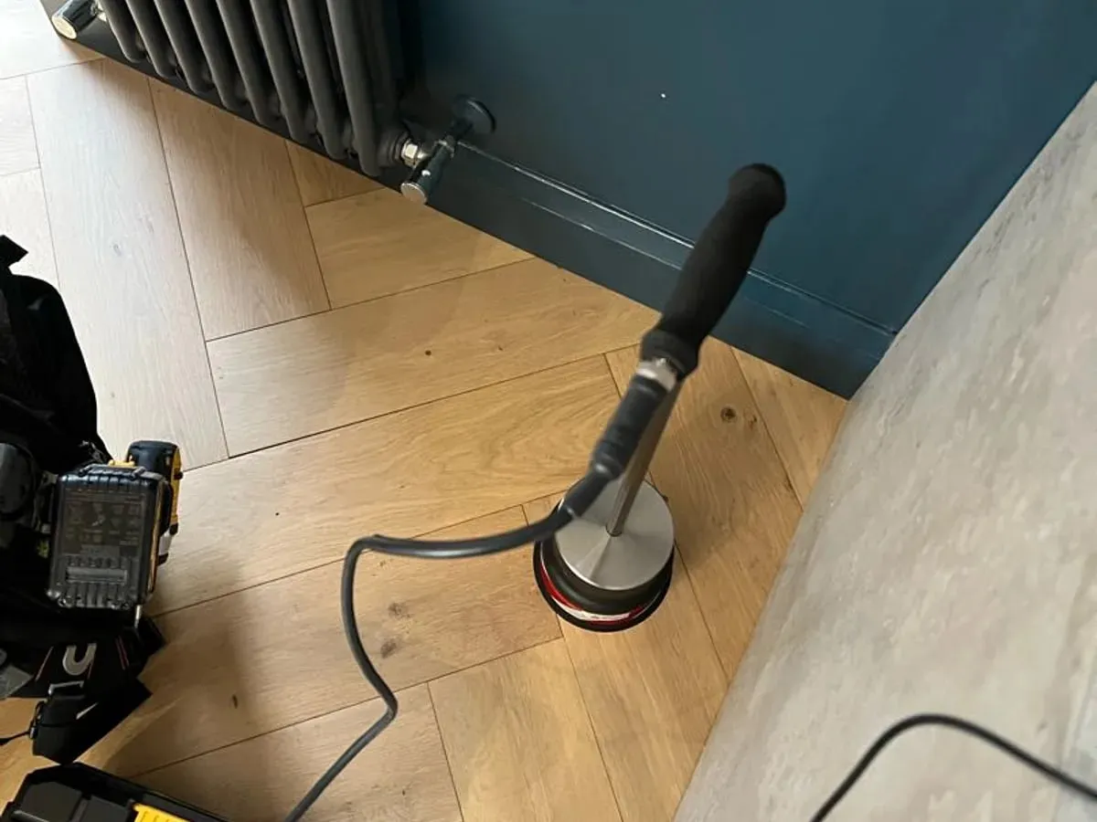 Tracer gas probe held against a wooden floor beside a radiator