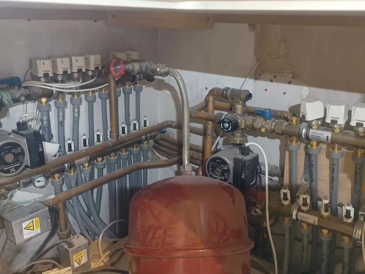 Two underfloor heating manifolds with pumps and an expansion vessel in a utility cupboard